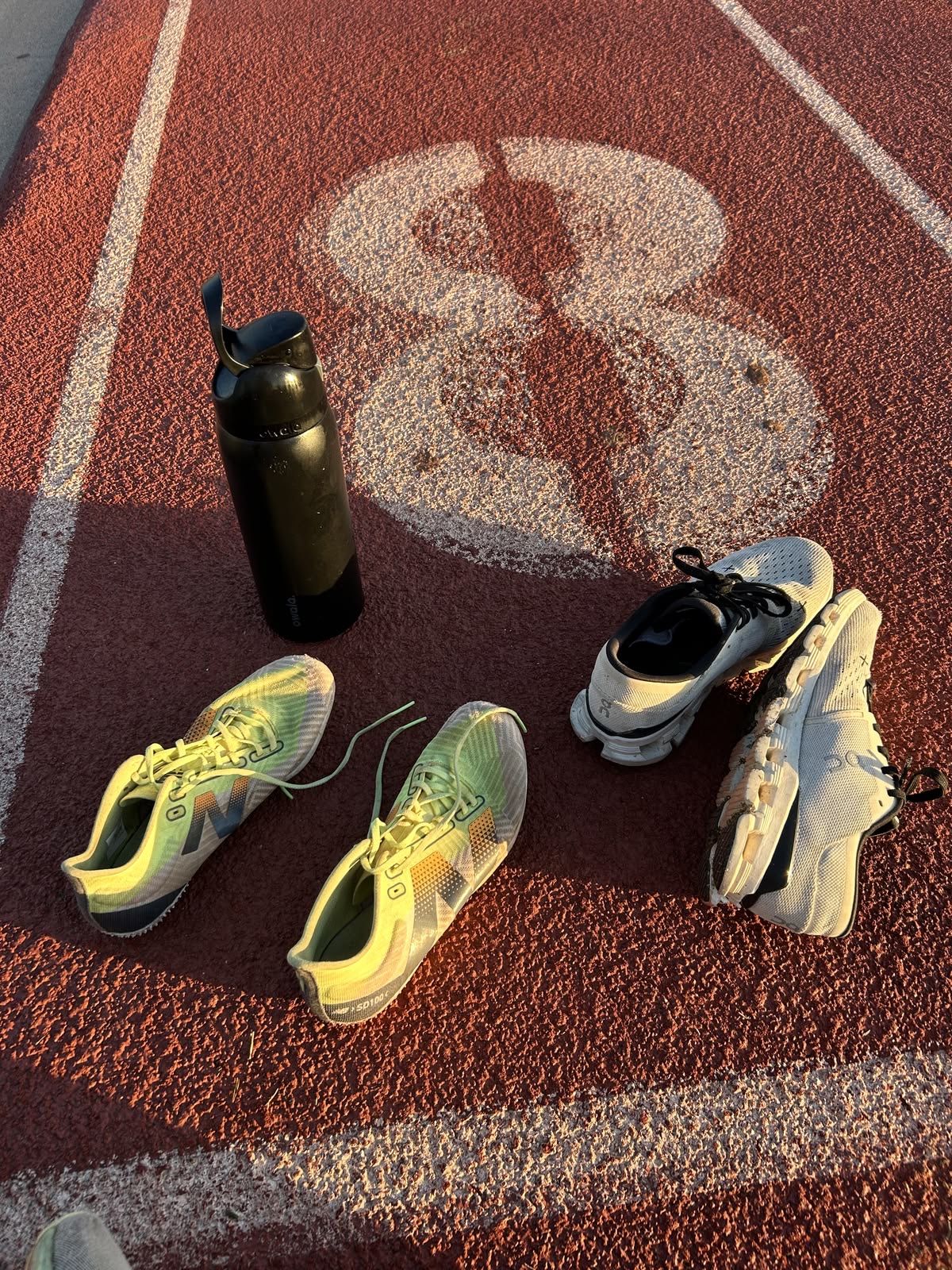 Laufschuhe und Flasche auf Tartanbahn